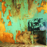 Blue-green paint peels from a water damaged wall