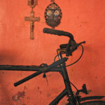 A bicycle leans on a rust coloured wall beneath relgious iconography