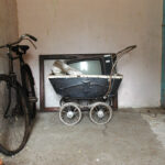A bicycle, pram bearing an old TV and a frame sit in the corner of a small room