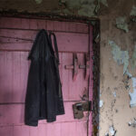 A worker's style jacket hangs on a pink painted cottage door