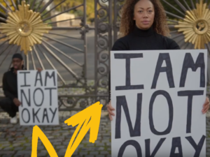 Two black performers hold placards stating "I am not OK".