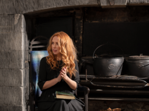 Lisa Lambe sits in a working inglenook, with her palms together as if addressing a small group.